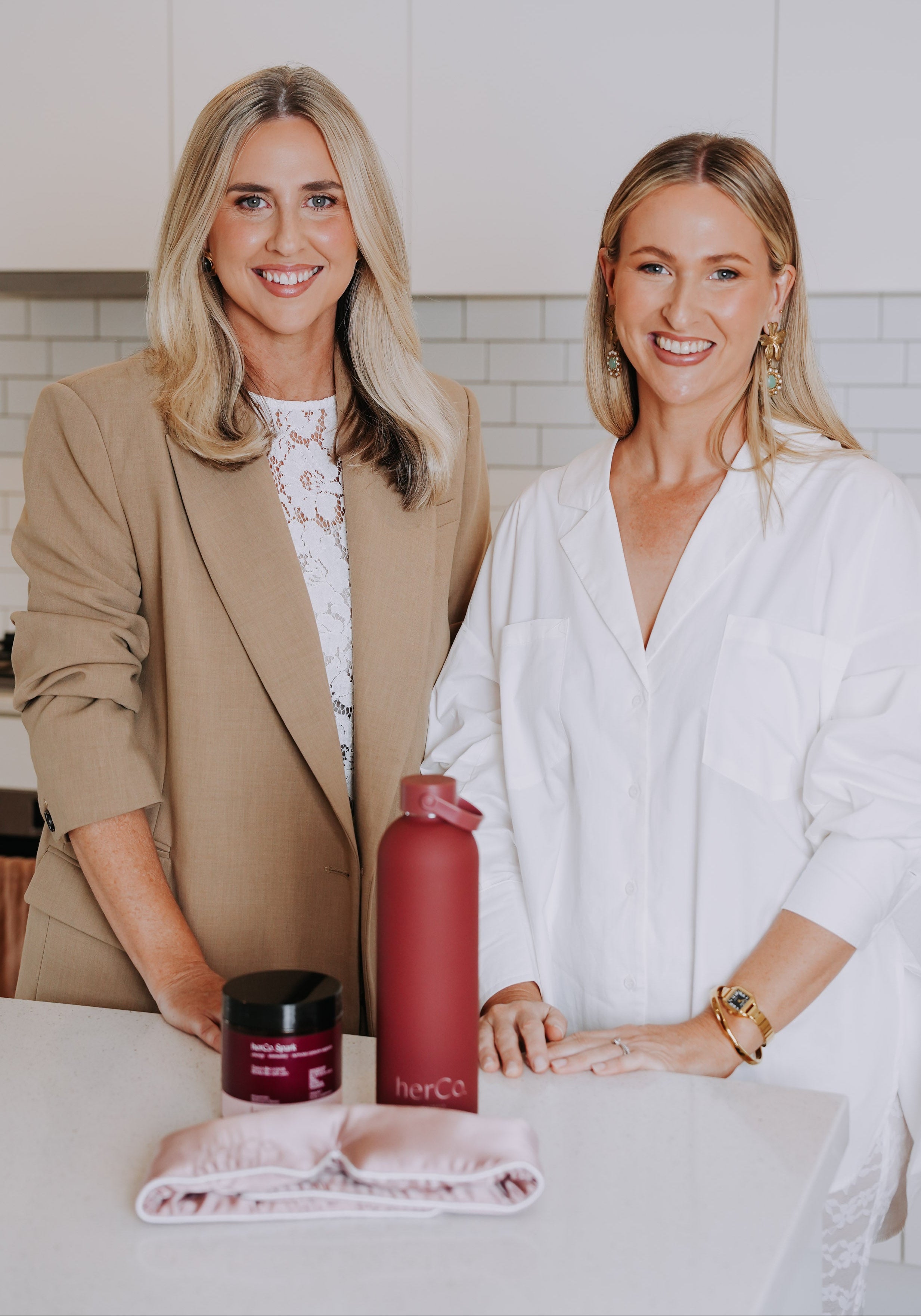 Two women standing in kitchen with herCo products on bench