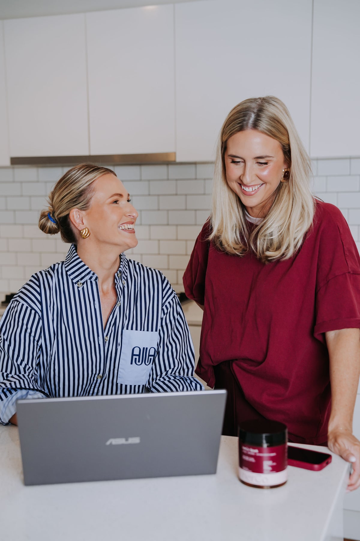 Two women in a kitchen looking at a laptop together.