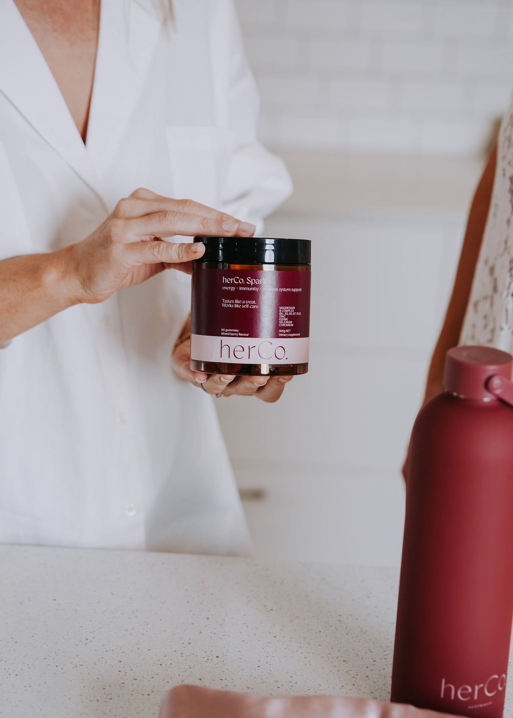 person holding a jar of herCo. Spark product. water bottle in background